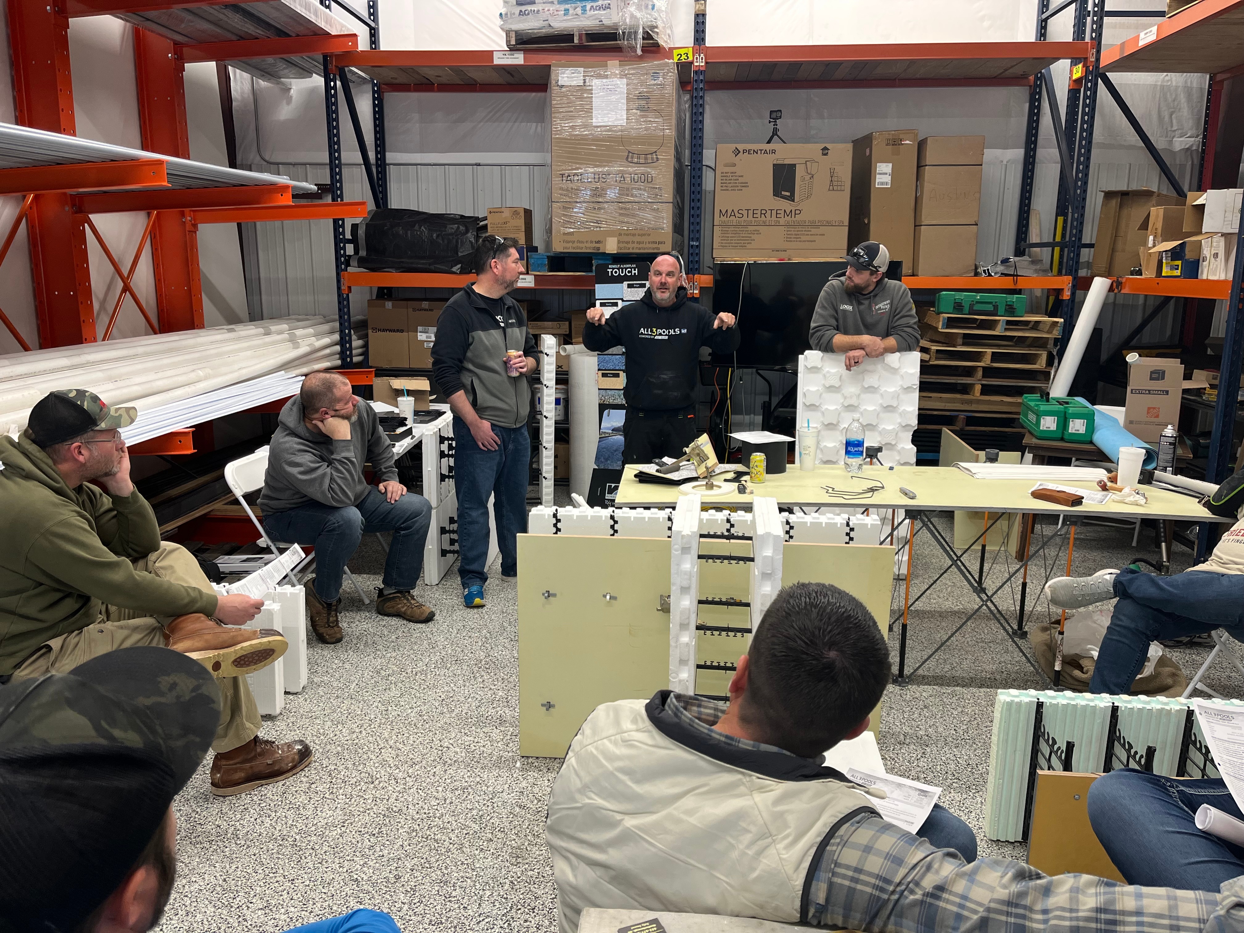 Aaron King teaching ICF pool construction with builders gathered around ICF demonstration blocks