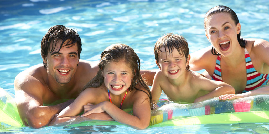 Young Family Relaxing In Swimming Pool Together